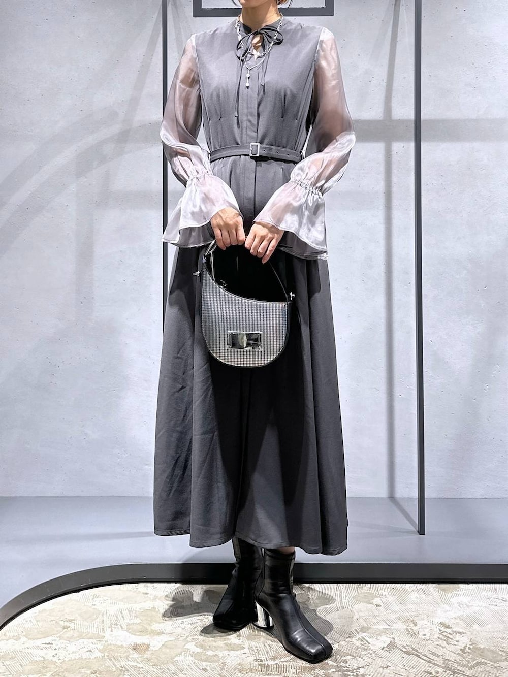 シルバー系のハンドバッグ、ブラック系のブーツ、グレー系のドレスを着用したレディースの秋コーディネートの5枚目の写真