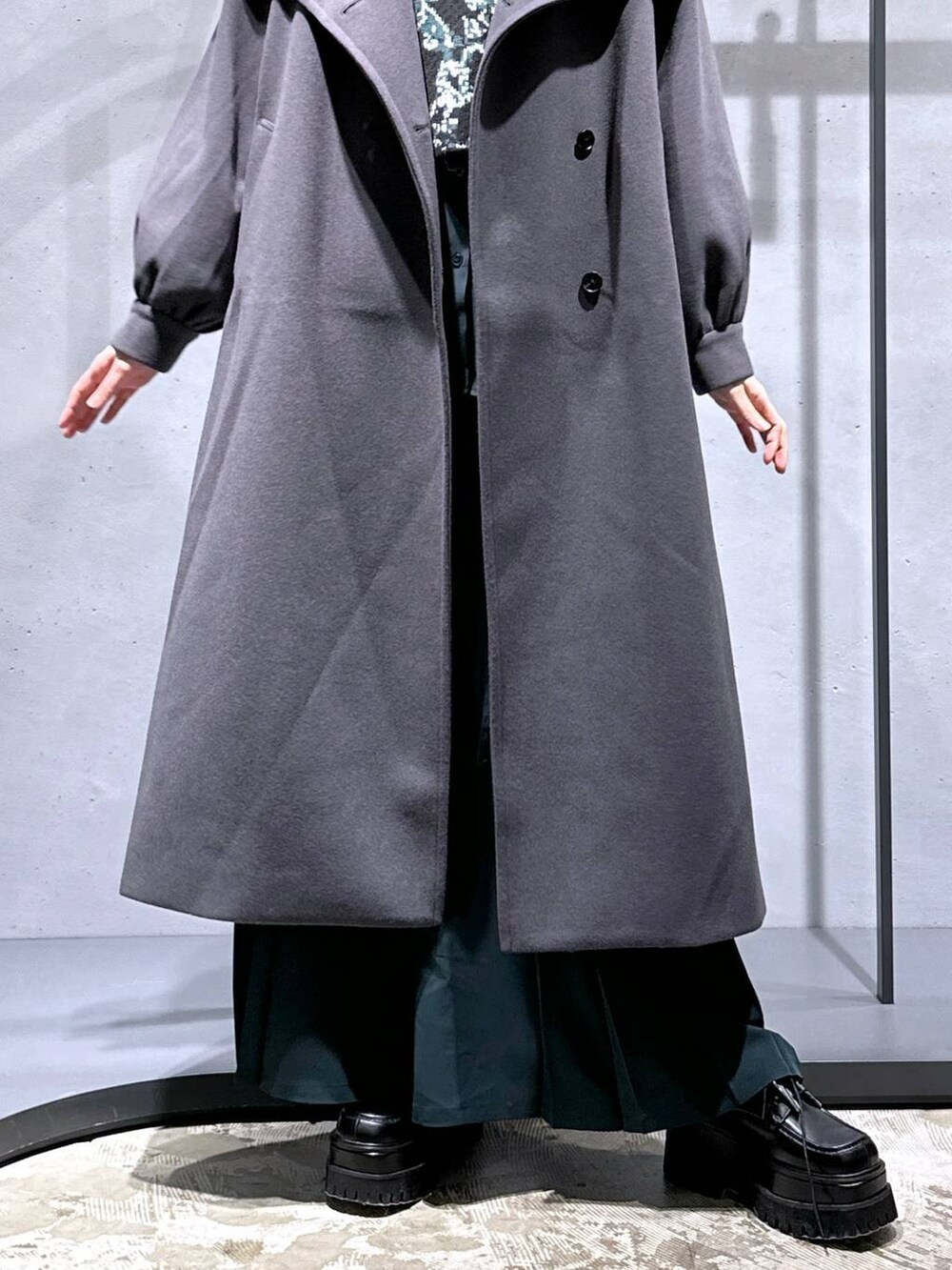 グレー系のチェスターコート、ブラック系のニット/セーター、グリーン系のシャツ/ブラウスを着用したレディースの秋コーディネートの6枚目の写真