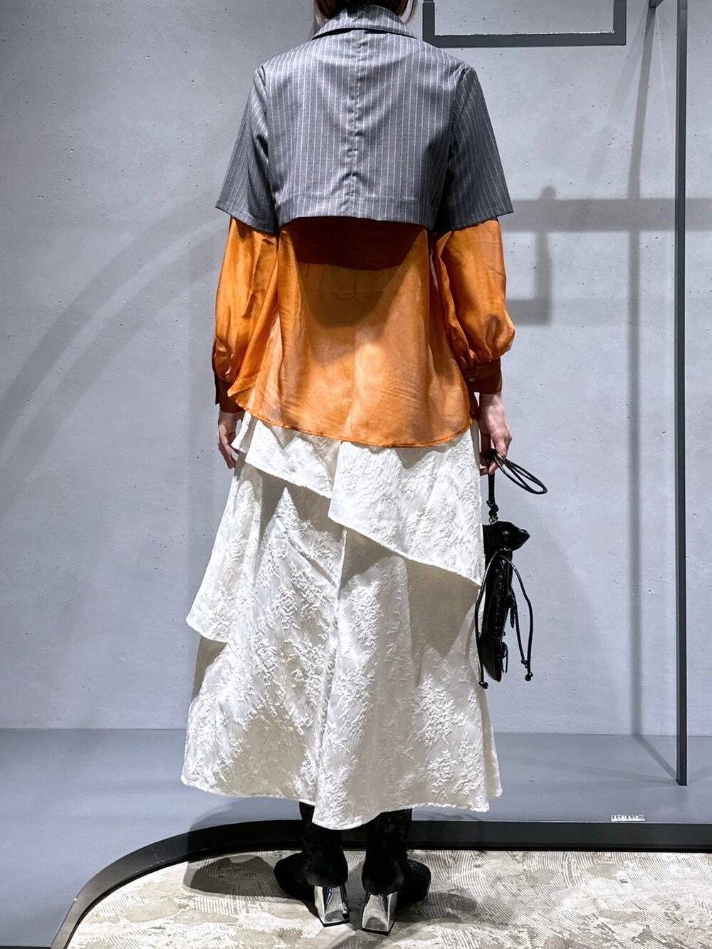 オレンジ系のシャツ/ブラウス、ホワイト系のスカート、ブラック系のブーツを着用したレディースの夏コーディネートの3枚目の写真