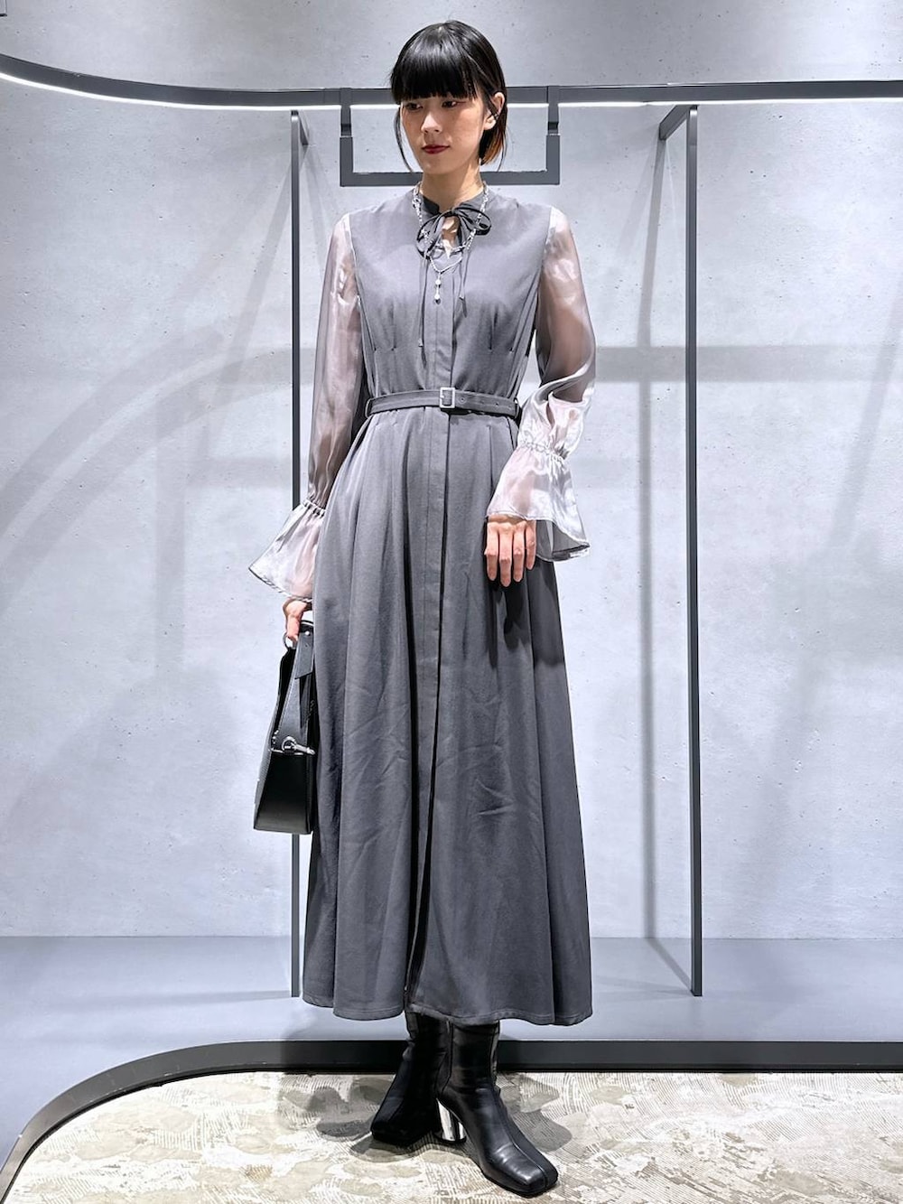 シルバー系のハンドバッグ、ブラック系のブーツ、グレー系のドレスを着用したレディースの秋コーディネートの2枚目の写真