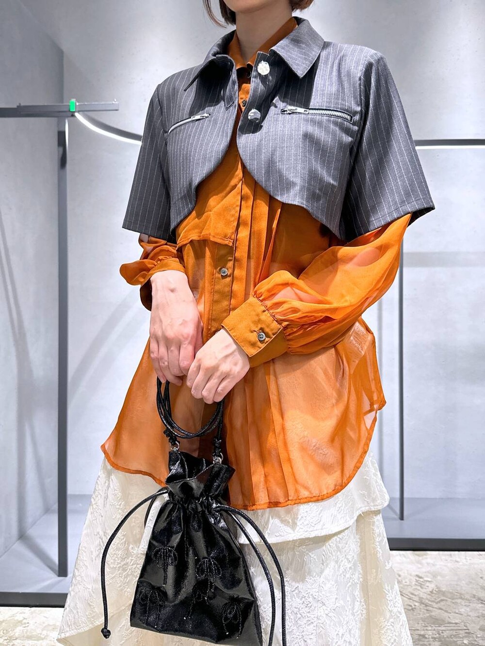 オレンジ系のシャツ/ブラウス、ホワイト系のスカート、ブラック系のブーツを着用したレディースの夏コーディネートの4枚目の写真