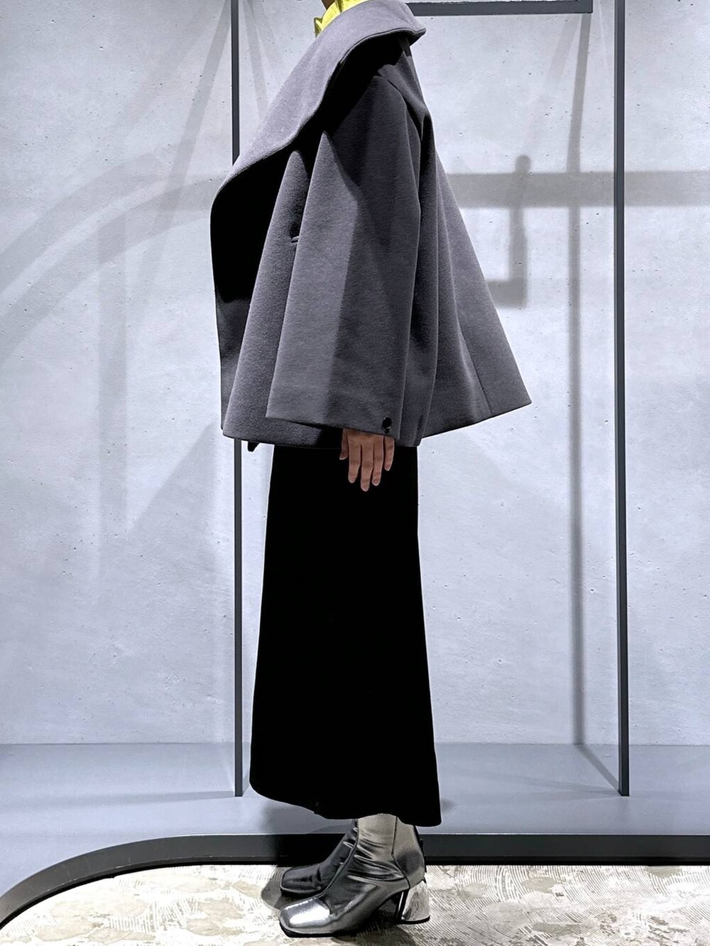 グレー系のチェスターコート、イエロー系のニット/セーター、シルバー系のブーツを着用したレディースの秋コーディネートの2枚目の写真