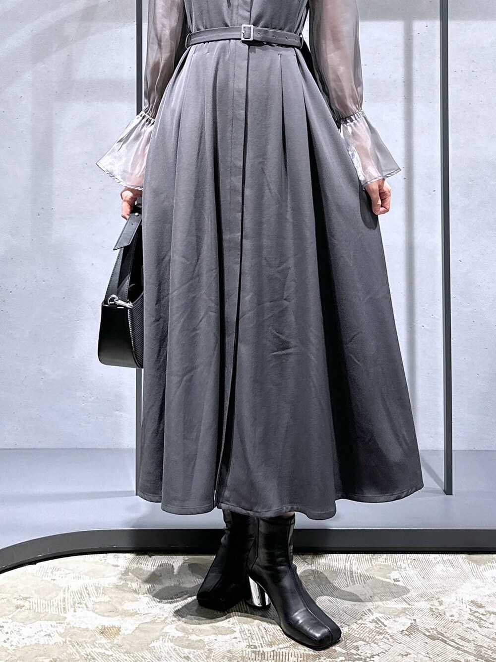 シルバー系のハンドバッグ、ブラック系のブーツ、グレー系のドレスを着用したレディースの秋コーディネートの7枚目の写真