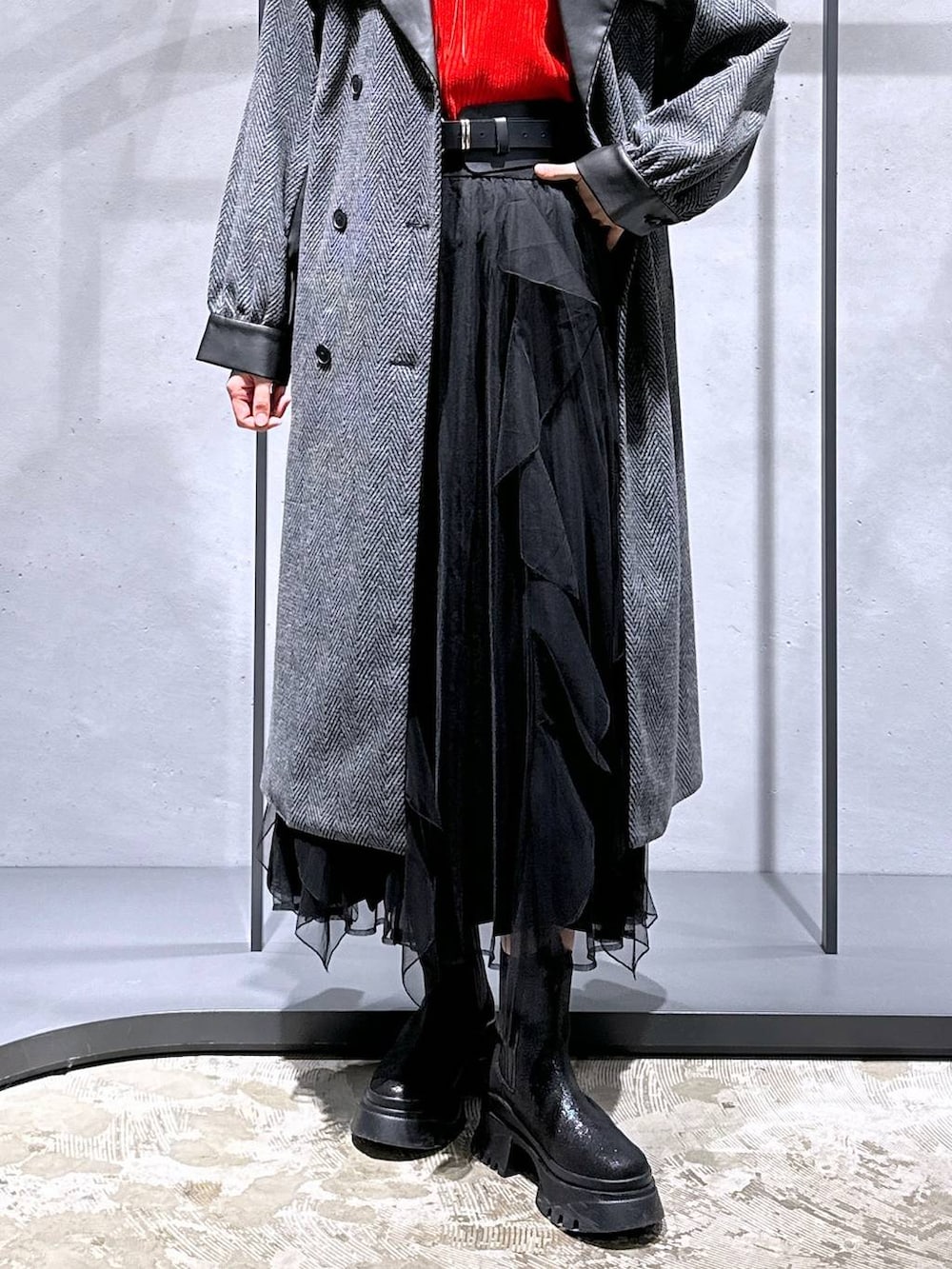 グレー系のチェスターコート、レッド系のニット/セーター、ブラック系のブーツを着用したレディースの冬コーディネートの6枚目の写真