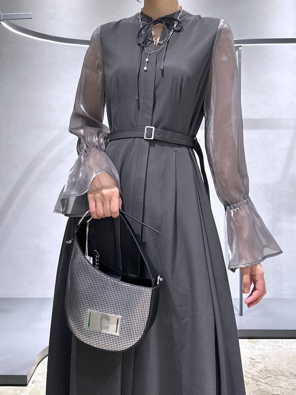 シルバー系のハンドバッグ、ブラック系のブーツ、グレー系のドレスを着用したレディースの秋コーディネートの6枚目の写真