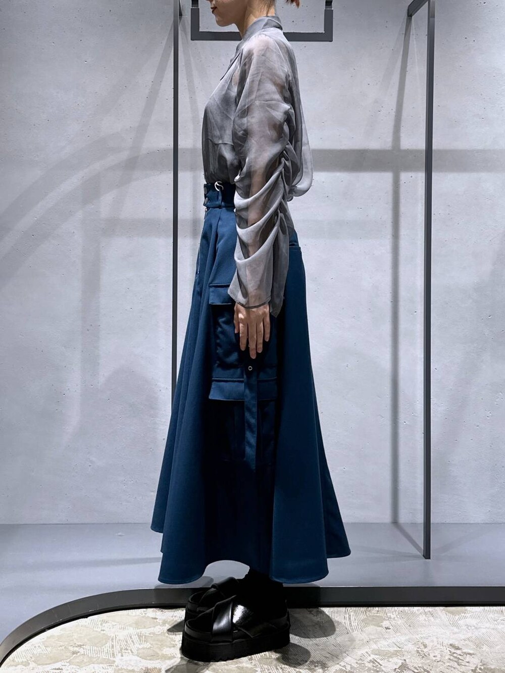 ブラック系のサンダル、ブルー系のスカート、シルバー系のネックレスを着用したレディースの春コーディネートの2枚目の写真