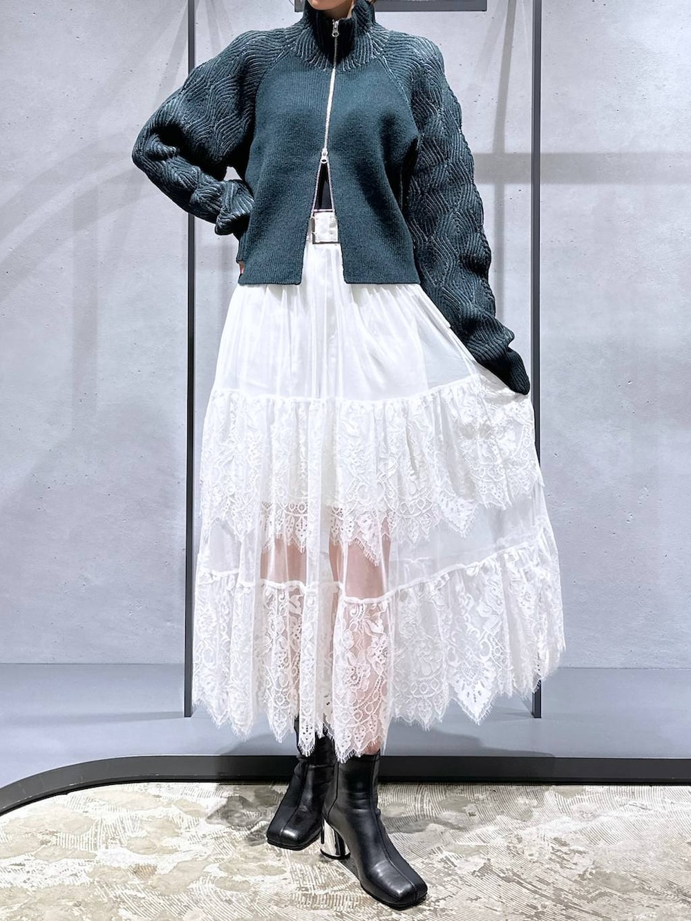 ブラック系のブーツ、グリーン系のカーディガン/ボレロ、ホワイト系のスカートを着用したレディースの秋コーディネートの4枚目の写真
