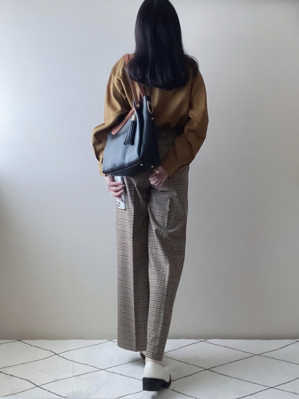 イエロー系のトップス、ベージュ系のパンツ、ブラック系のトートバッグを着用したレディースの秋コーディネートの2枚目の写真