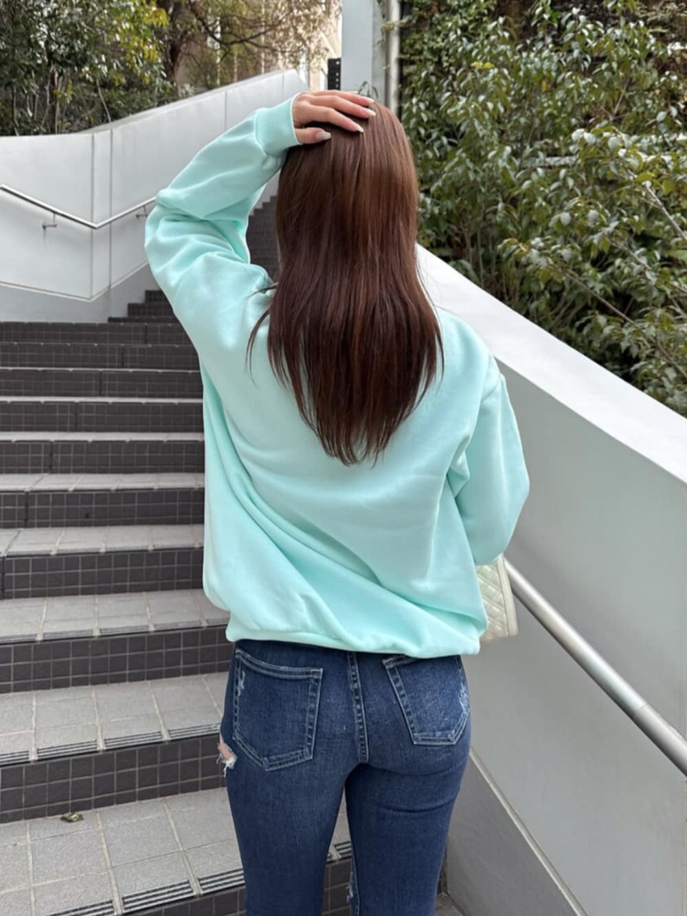 ブルー系のデニムパンツ、ホワイト系のショルダーバッグ、グリーン系のスウェットを着用したレディースの冬コーディネートの6枚目の写真