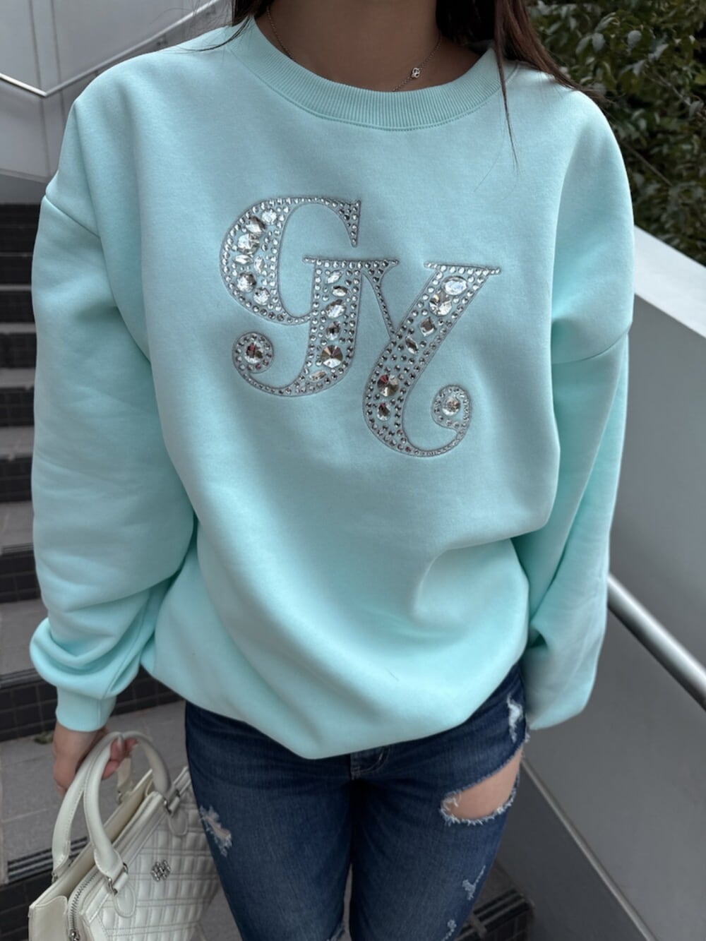 ブルー系のデニムパンツ、ホワイト系のショルダーバッグ、グリーン系のスウェットを着用したレディースの冬コーディネートの7枚目の写真