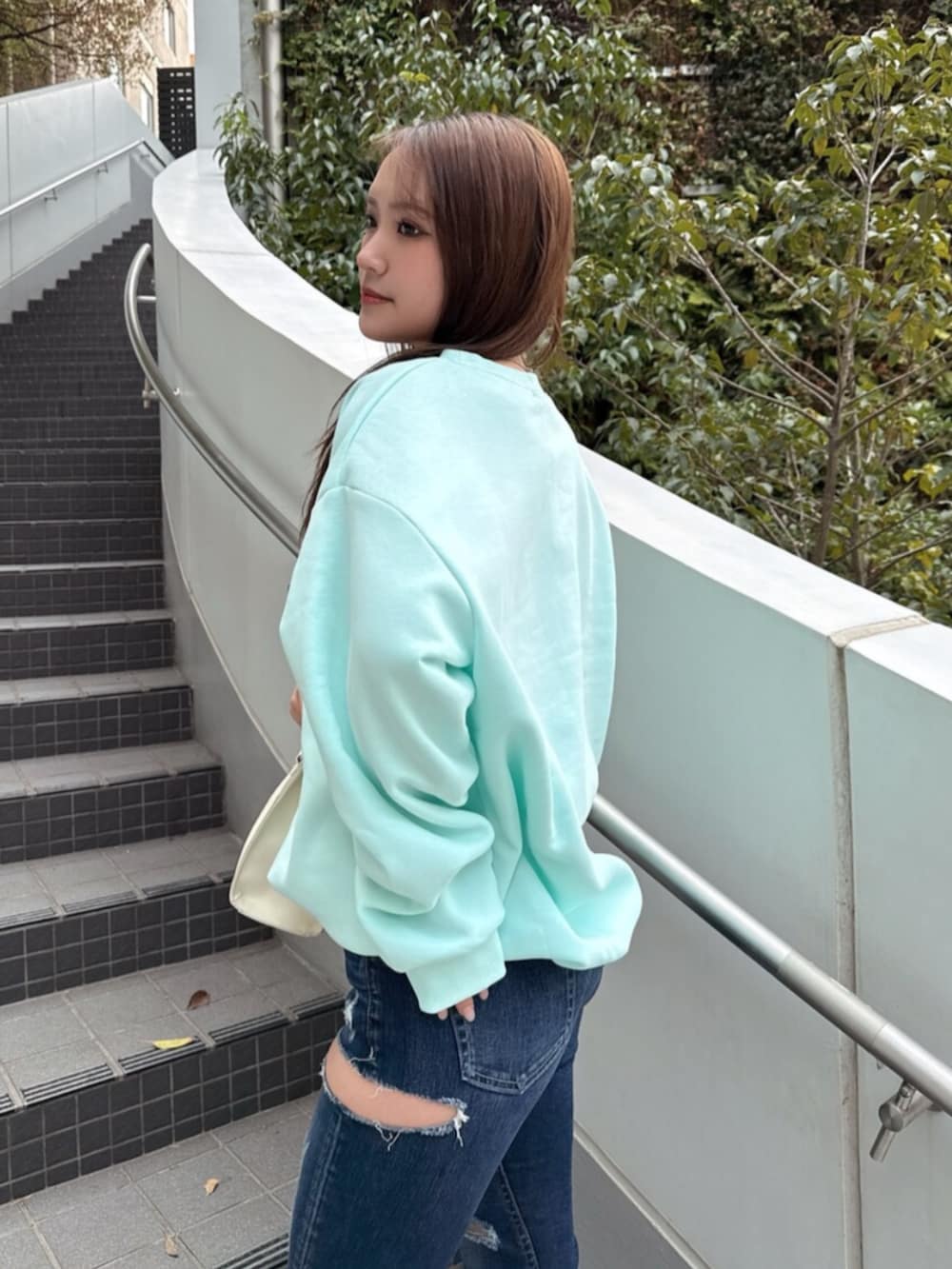 ブルー系のデニムパンツ、ホワイト系のショルダーバッグ、グリーン系のスウェットを着用したレディースの冬コーディネートの5枚目の写真