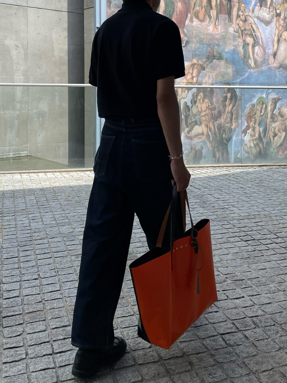 ホワイト系のポロシャツ、ブルー系のデニムパンツ、オレンジ系のトートバッグを着用したメンズの夏コーディネートの2枚目の写真