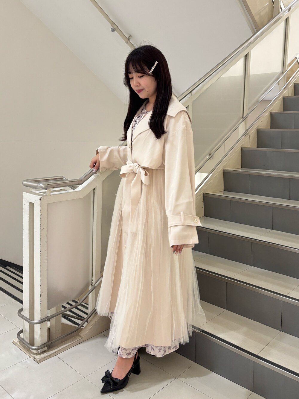 ブラック系のパンプス、ホワイト系のトレンチコート、ホワイト系のショルダーバッグを着用したレディースの春コーディネートの2枚目の写真