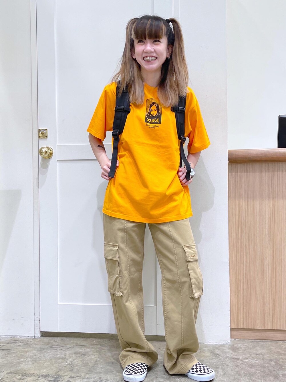 レッド系のバックパック/リュック、オレンジ系のTシャツ/カットソー、ベージュ系のカーゴパンツを着用したレディースの夏コーディネートの2枚目の写真