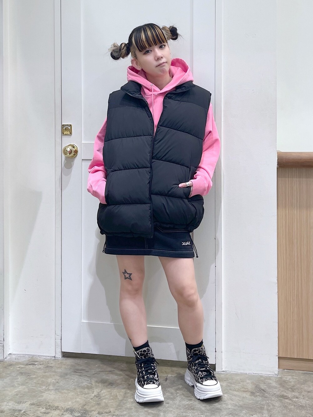 ブラック系のダウンベスト、ピンク系のパーカー、ブラック系のスカートを着用したレディースの秋コーディネートの2枚目の写真