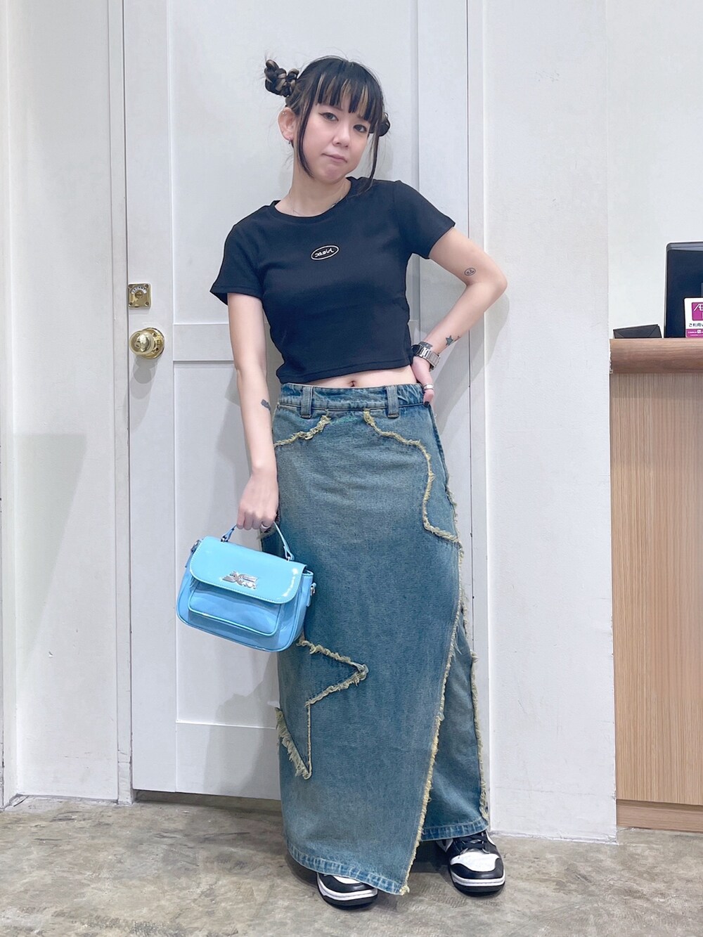 ブラック系のTシャツ/カットソー、ブルー系のデニムスカート、ブルー系のショルダーバッグを着用したレディースの夏コーディネートの2枚目の写真