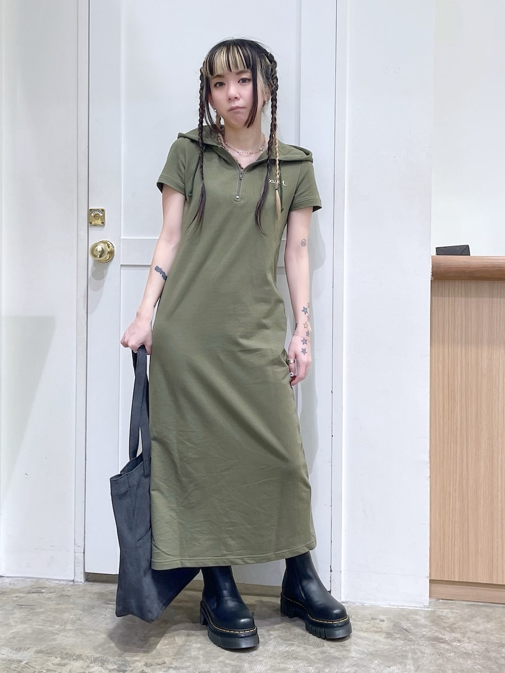 グレー系のトートバッグ、グリーン系のワンピース、ブラック系のブーツを着用したレディースの春コーディネートの2枚目の写真