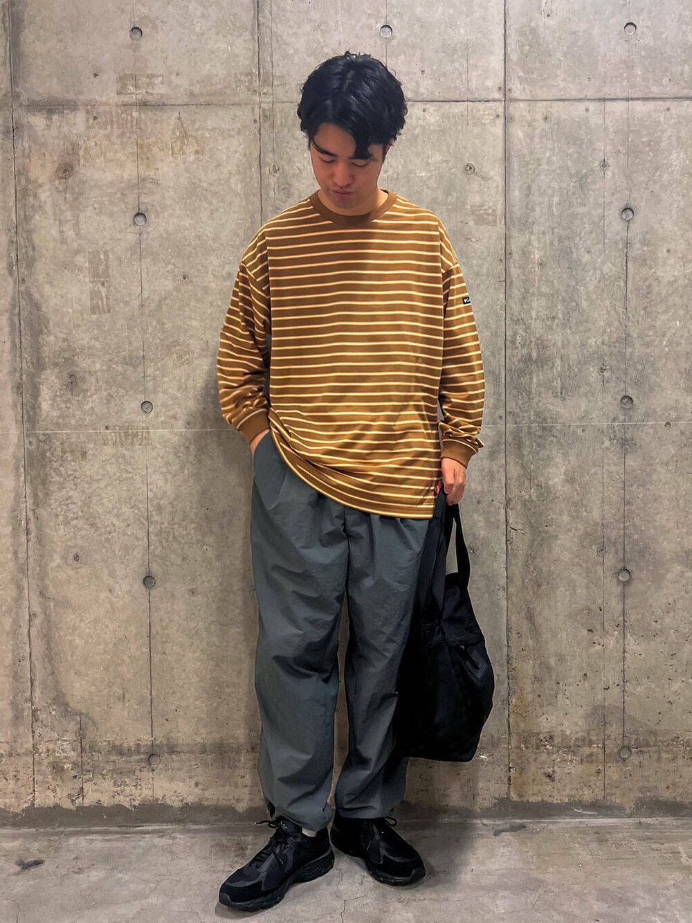 グレー系のその他パンツ、ブラック系のトートバッグ、ベージュ系のTシャツ/カットソーを着用したメンズの秋コーディネートの2枚目の写真