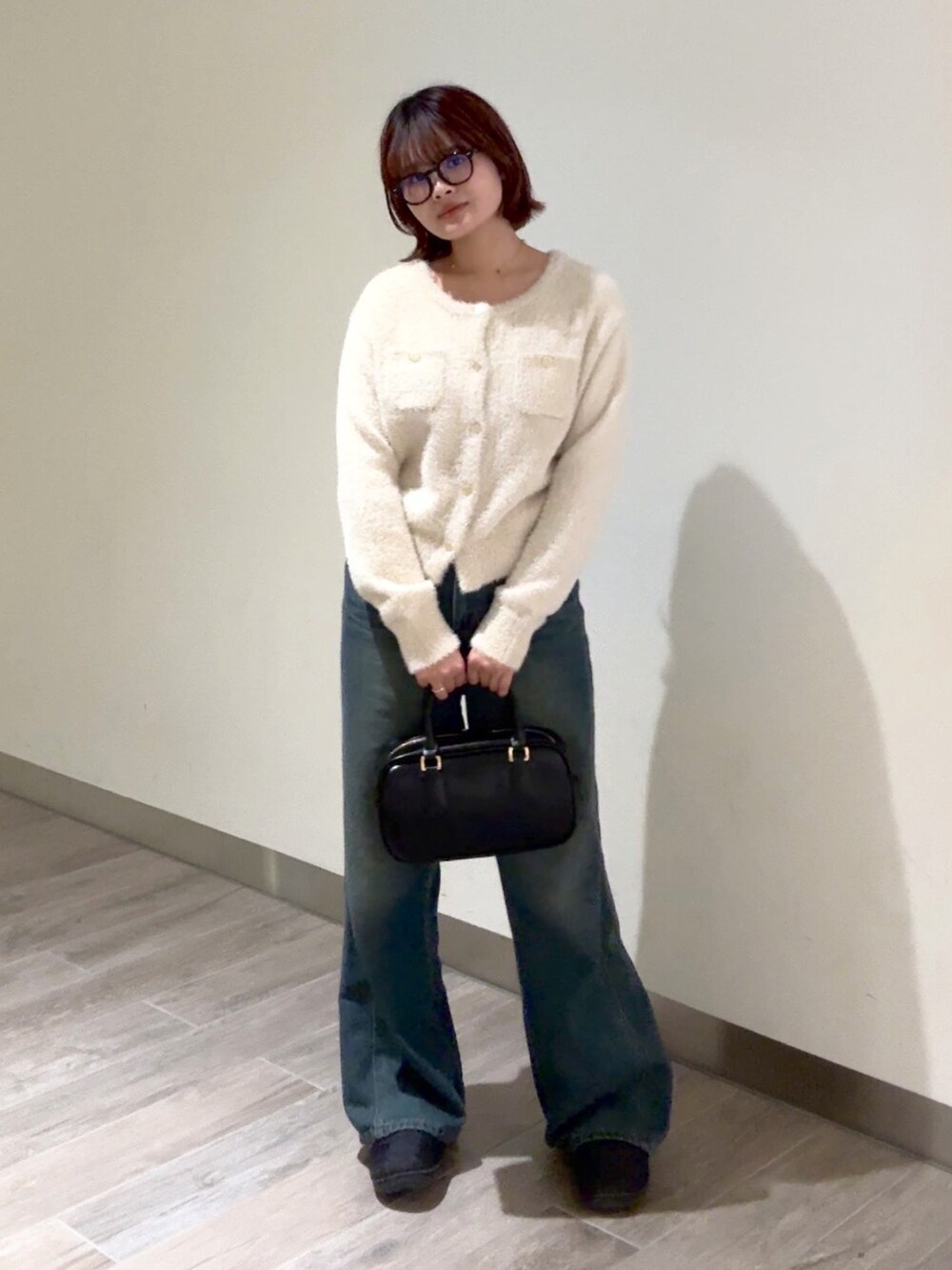 ブルー系のデニムパンツ、ブラック系のハンドバッグ、ベージュ系のニット/セーターを着用したレディースの冬コーディネートの2枚目の写真