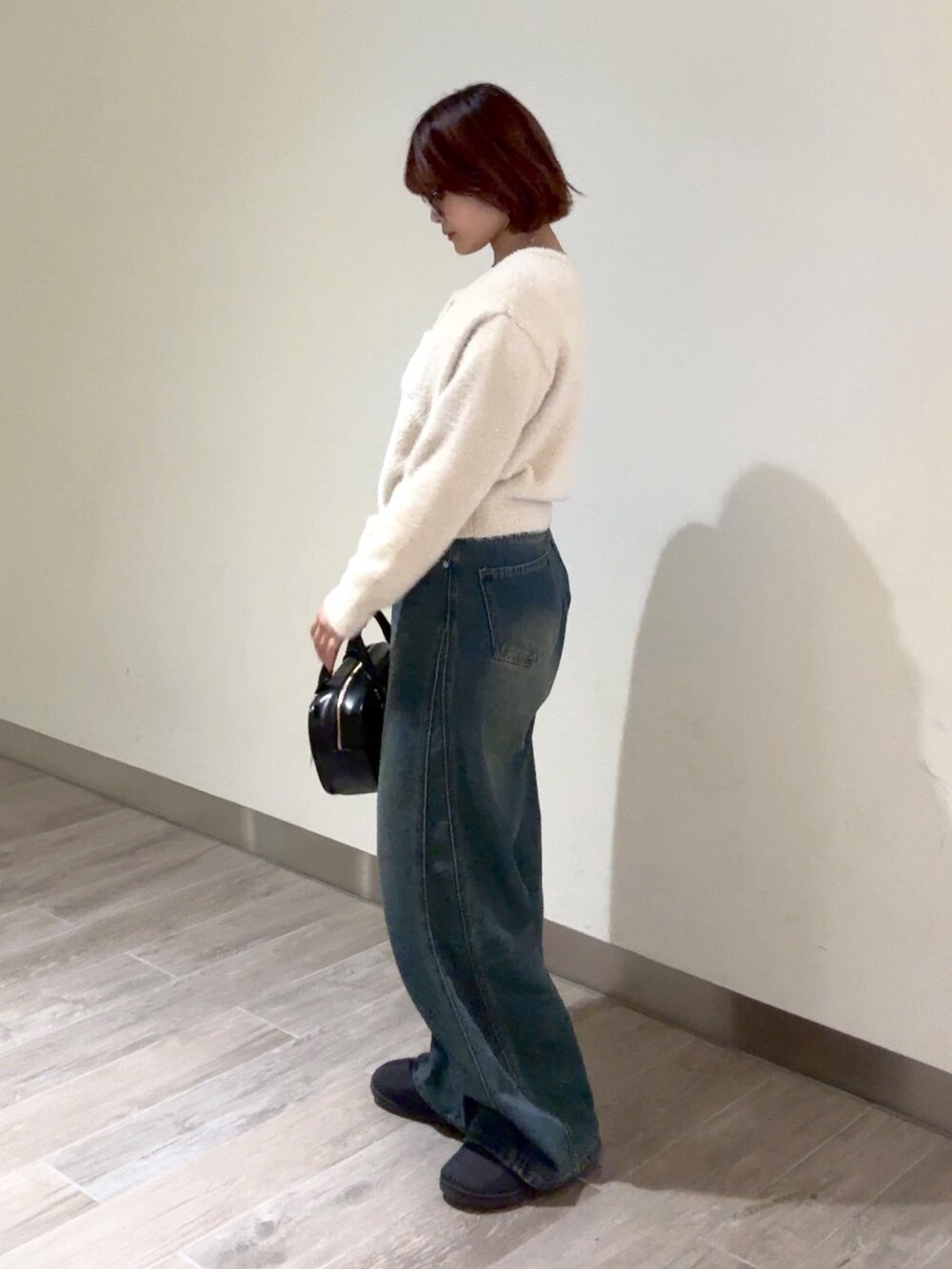 ブルー系のデニムパンツ、ブラック系のハンドバッグ、ベージュ系のニット/セーターを着用したレディースの冬コーディネートの4枚目の写真