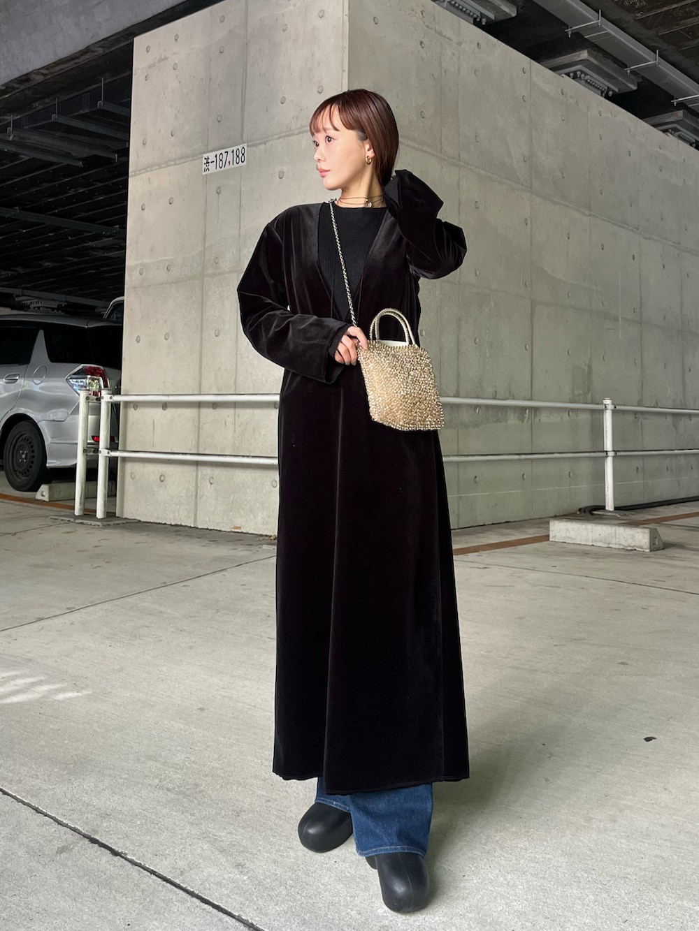 ブラック系のワンピース、ベージュ系のバッグ、ブルー系のデニムパンツを着用したレディースの秋コーディネートの2枚目の写真