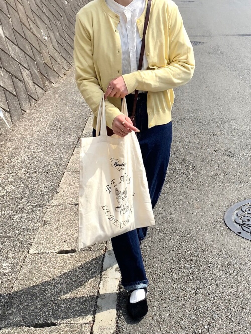 ブラウン系のショルダーバッグ、ブラック系のバレエシューズ、ブルー系のデニムパンツを着用したレディースの春コーディネートの2枚目の写真