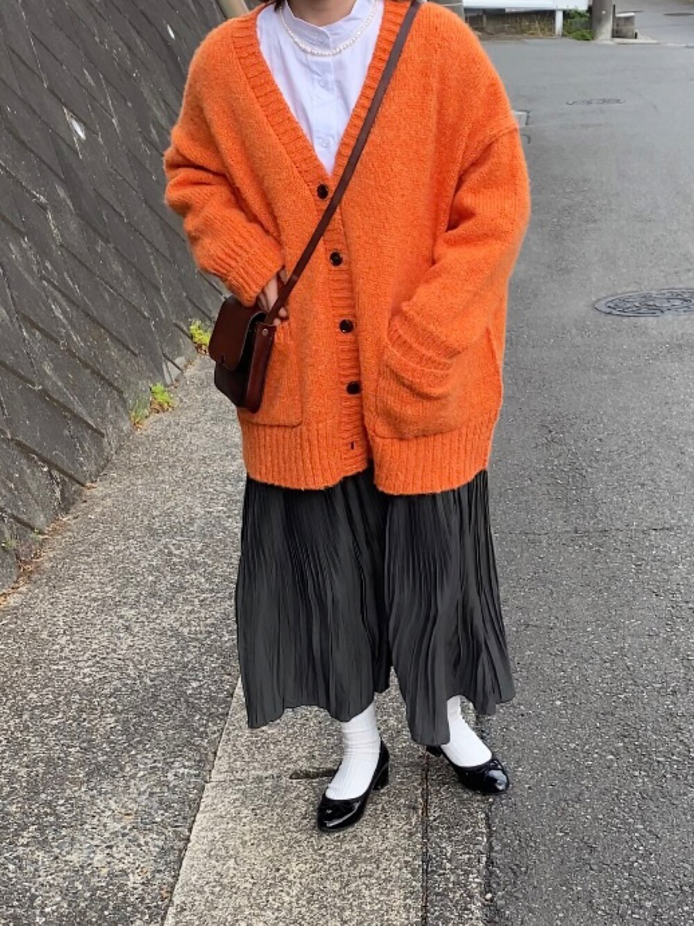 グリーン系のスカート、ブラウン系のショルダーバッグ、オレンジ系のカーディガン/ボレロを着用したレディースの春コーディネートの3枚目の写真