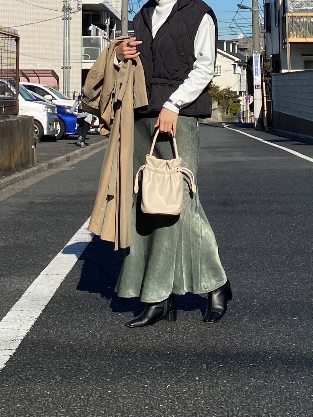 ブラック系のベスト、ベージュ系のトレンチコート、ホワイト系のTシャツ/カットソーを着用したレディースの冬コーディネートの2枚目の写真