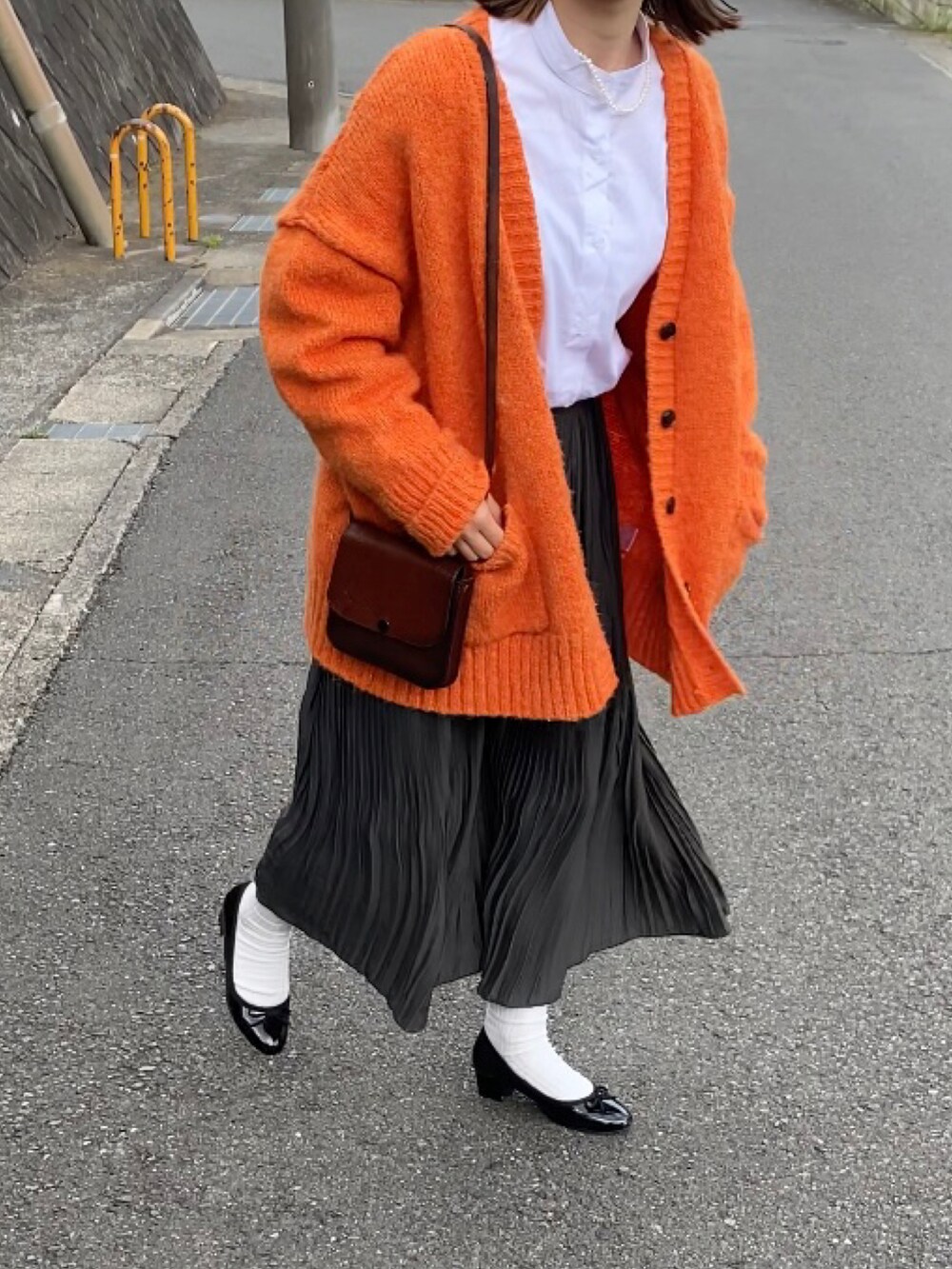 グリーン系のスカート、ブラウン系のショルダーバッグ、オレンジ系のカーディガン/ボレロを着用したレディースの春コーディネートの2枚目の写真