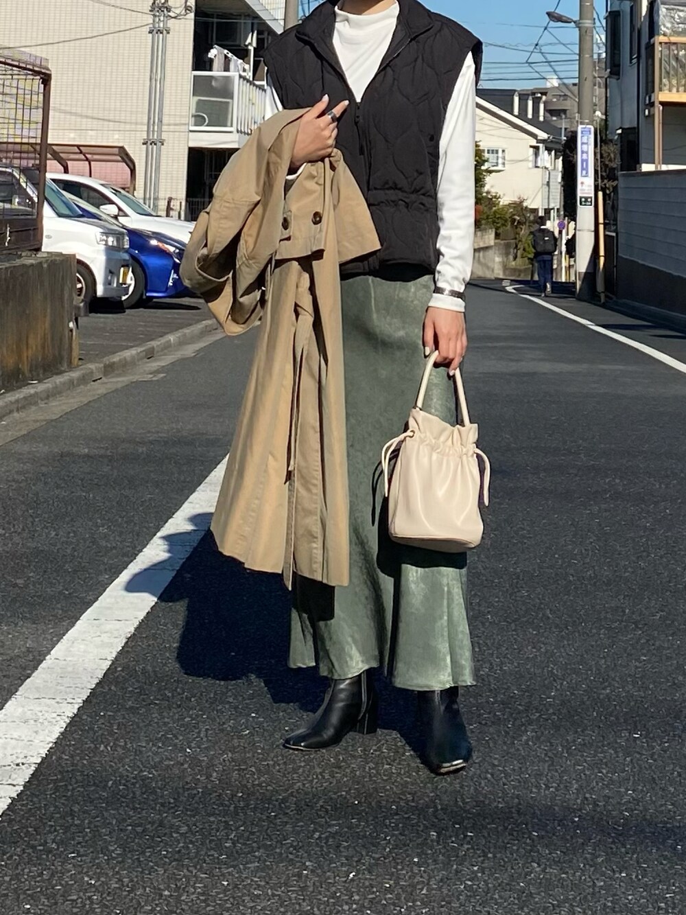 ブラック系のベスト、ベージュ系のトレンチコート、ホワイト系のTシャツ/カットソーを着用したレディースの冬コーディネートの3枚目の写真