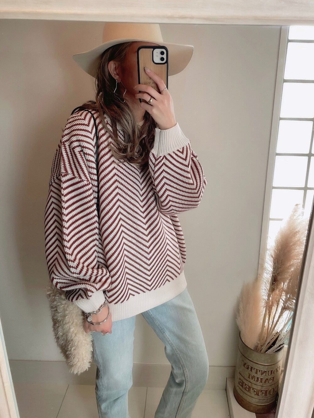 オレンジ系のニット/セーター、ホワイト系のショルダーバッグ、ホワイト系のハットを着用したレディースの冬コーディネートの2枚目の写真