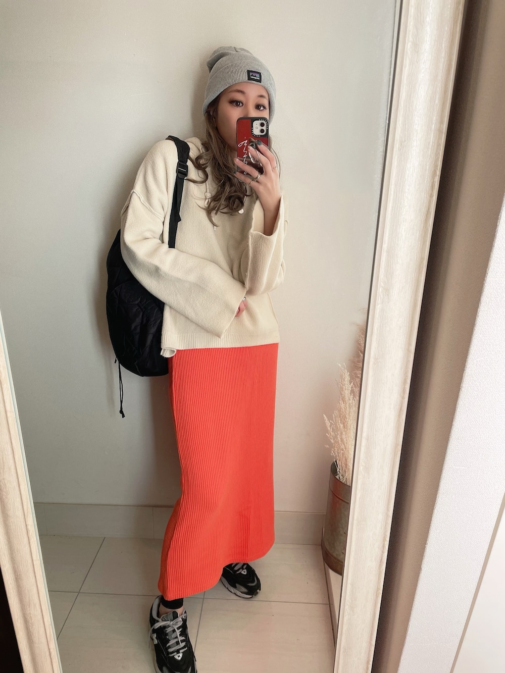 オレンジ系のスカート、ブラック系のバックパック/リュック、ブラック系のスニーカーを着用したレディースの冬コーディネートの2枚目の写真