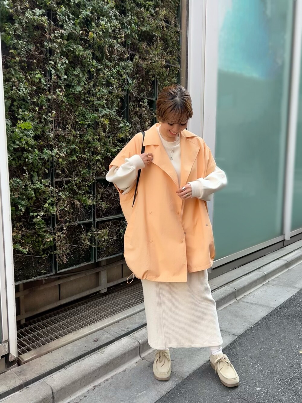 オレンジ系のポンチョ、ベージュ系のスカート、ベージュ系のモカシン/デッキシューズを着用したレディースの春コーディネートの4枚目の写真