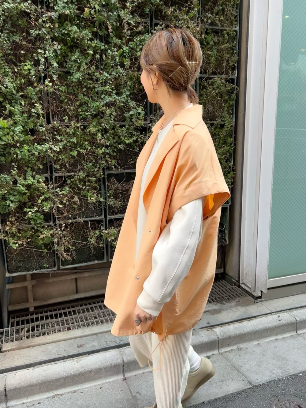 オレンジ系のポンチョ、ベージュ系のスカート、ベージュ系のモカシン/デッキシューズを着用したレディースの春コーディネートの3枚目の写真