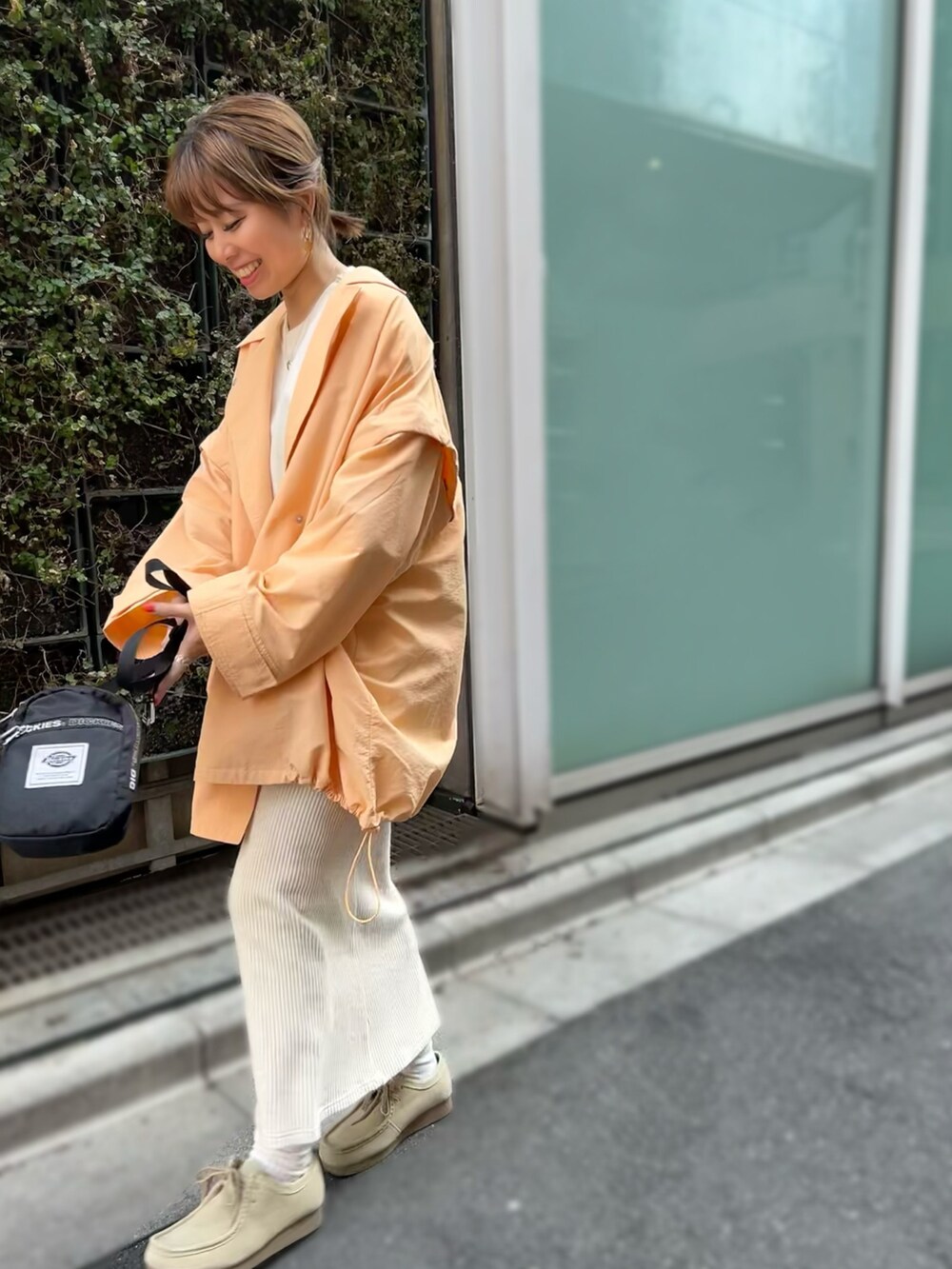 オレンジ系のポンチョ、ベージュ系のスカート、ベージュ系のモカシン/デッキシューズを着用したレディースの春コーディネートの2枚目の写真