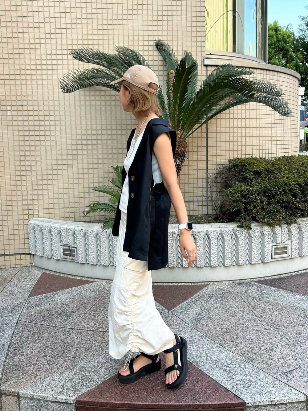 ブラック系のベスト、ブラック系のトートバッグ、ホワイト系のスカートを着用したレディースの夏コーディネートの3枚目の写真