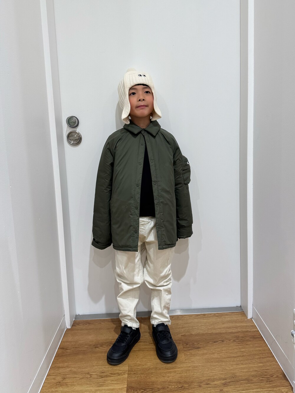 グリーン系のジャケット/アウター、ブラック系のスニーカー、ホワイト系のニットキャップ/ビーニーを着用したキッズの冬コーディネートの2枚目の写真