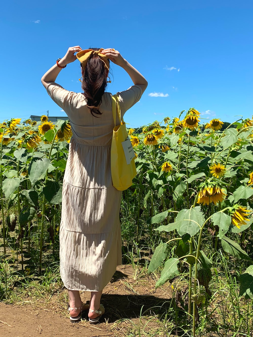 ベージュ系のワンピース、ベージュ系のトートバッグ、ホワイト系のサンダルを着用したレディースの夏コーディネートの2枚目の写真
