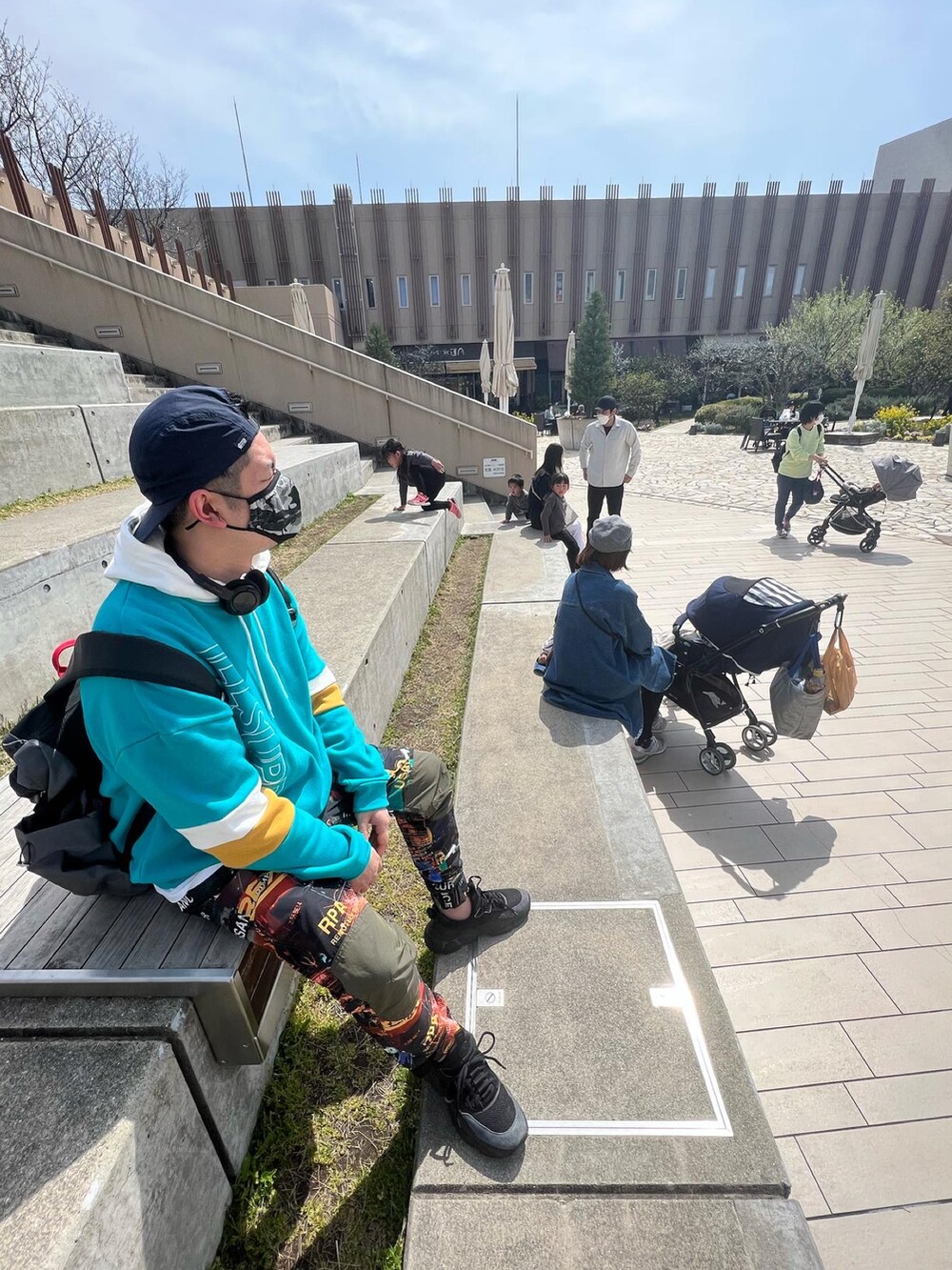 ブルー系のパーカー、オレンジ系のパンツ、ブラック系のスニーカーを着用したメンズの春コーディネートの2枚目の写真