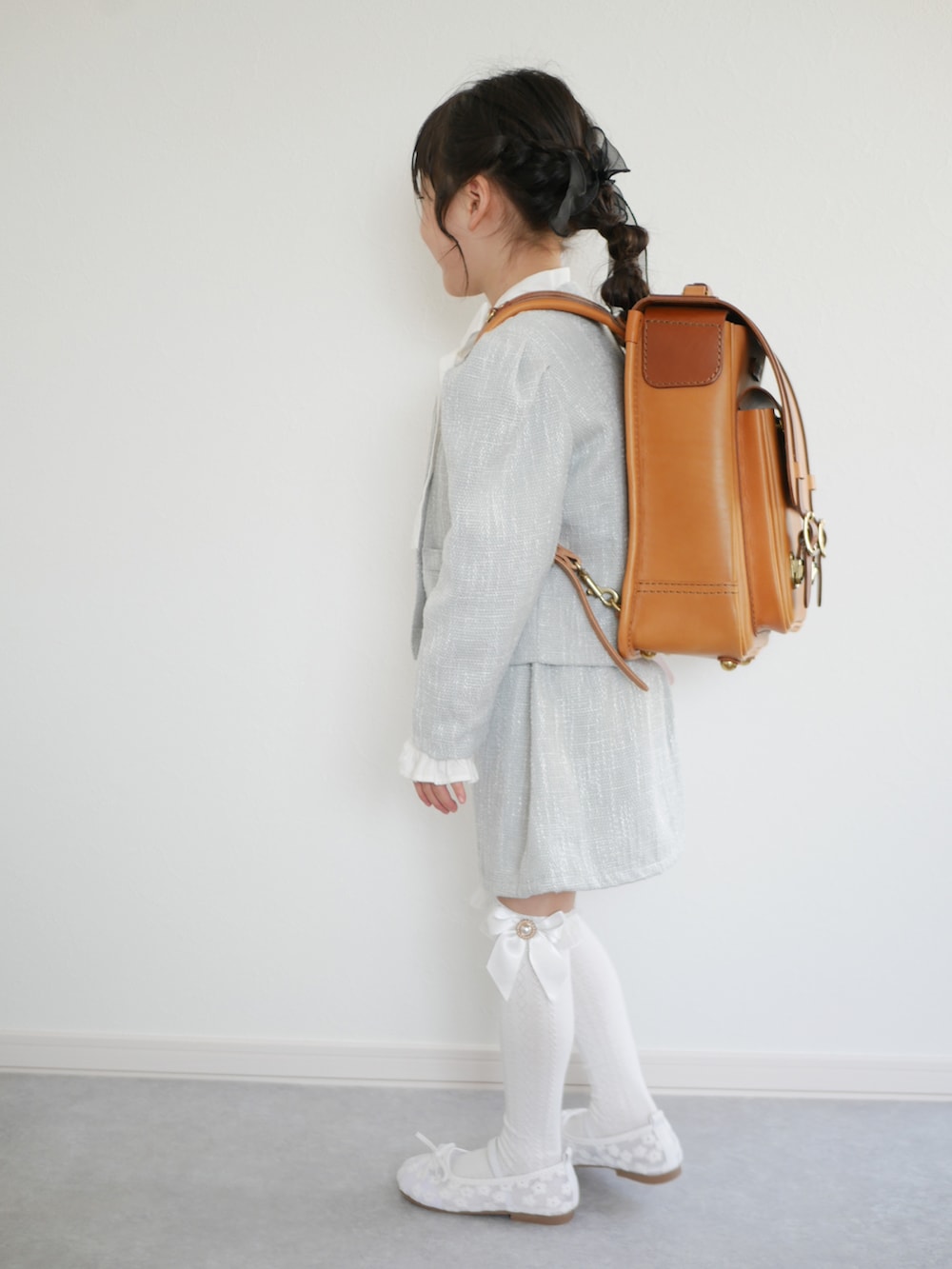 ホワイト系のバレエシューズ、グリーン系のノーカラーコート、ブラック系のバッグを着用したキッズの春コーディネートの2枚目の写真