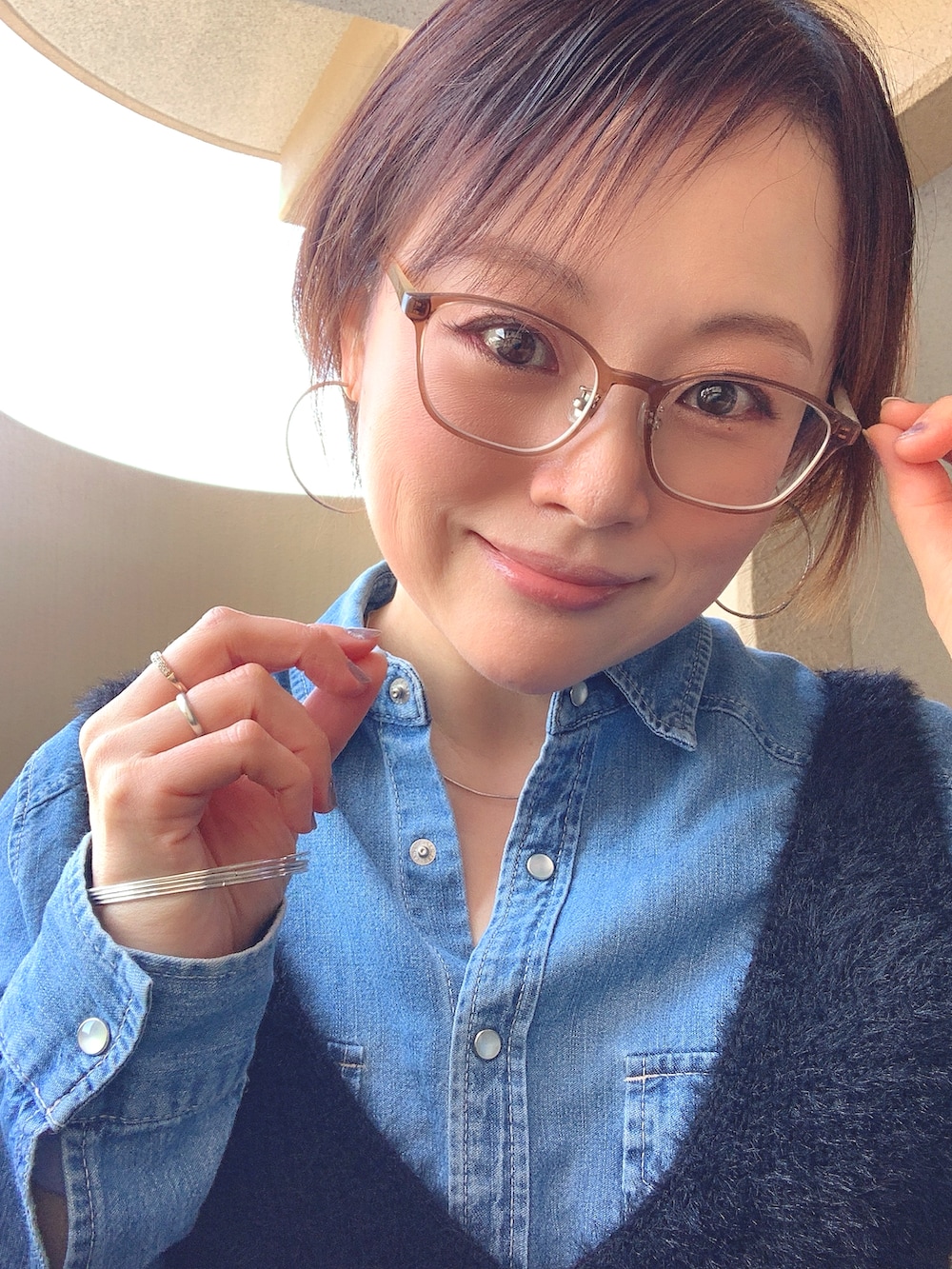 ブラック系のベスト、ブルー系のシャツ/ブラウス、ブルー系のデニムパンツを着用したレディースの春コーディネートの2枚目の写真