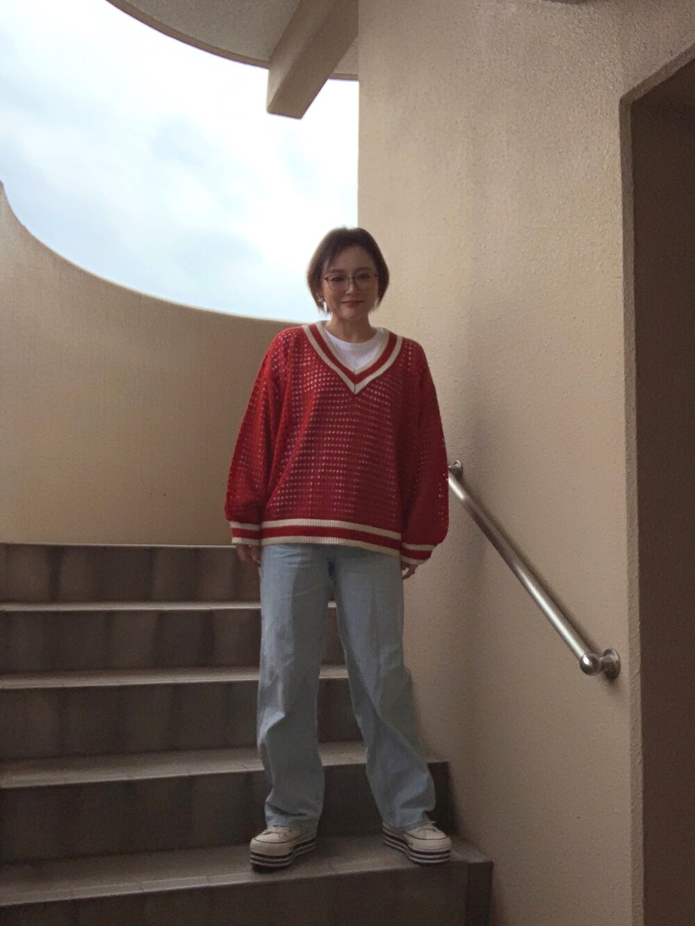 レッド系のニット/セーター、ホワイト系のTシャツ/カットソー、ブルー系のデニムパンツを着用したレディースの春コーディネートの2枚目の写真