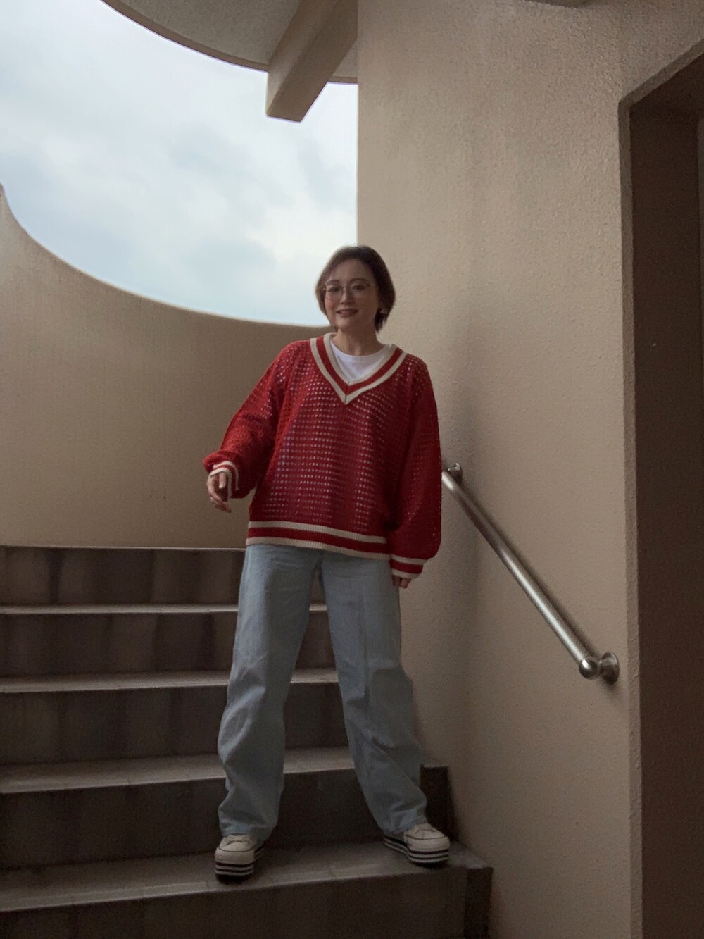 レッド系のニット/セーター、ホワイト系のTシャツ/カットソー、ブルー系のデニムパンツを着用したレディースの春コーディネートの3枚目の写真