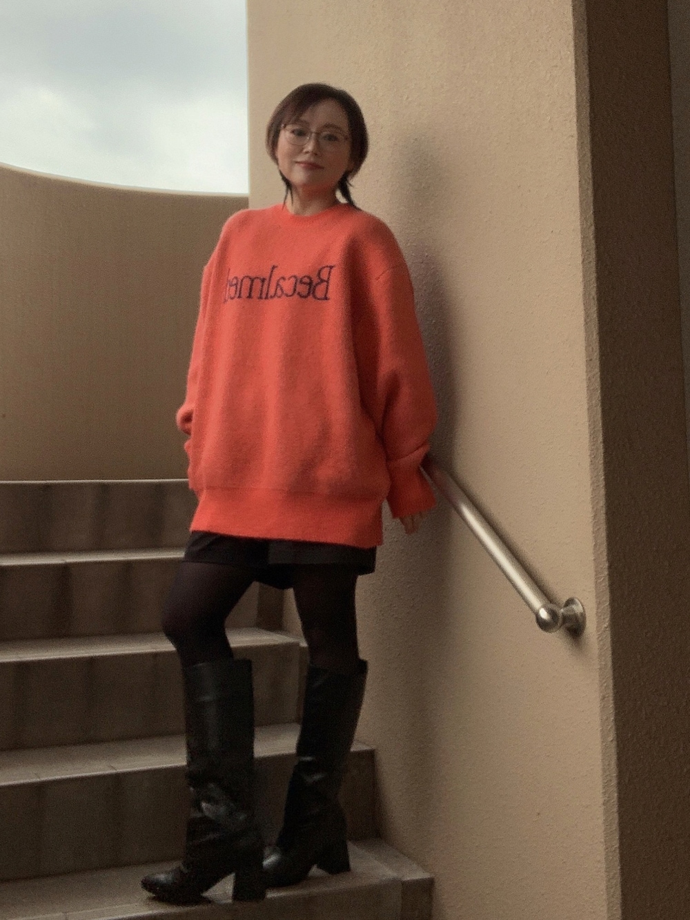 オレンジ系のニット/セーター、ブラック系のチノパンツ、ブラック系のブーツを着用したレディースの冬コーディネートの2枚目の写真