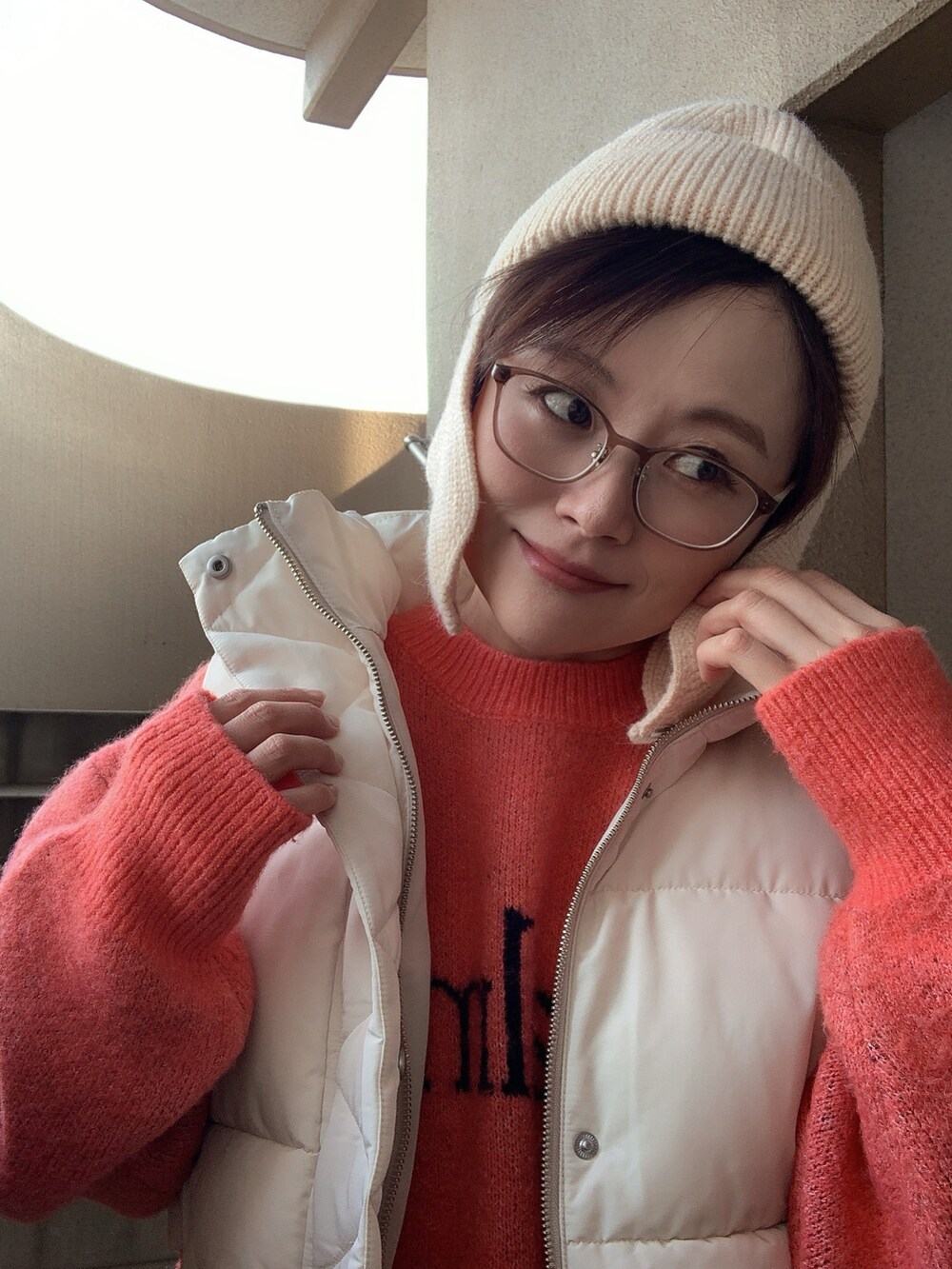 ホワイト系のダウンベスト、オレンジ系のニット/セーター、ホワイト系のその他パンツを着用したレディースの冬コーディネートの2枚目の写真