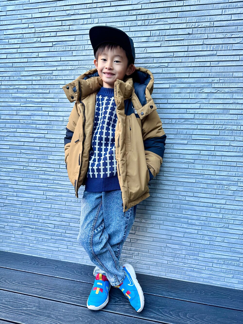 ベージュ系のダウンジャケット/コート、ブルー系のニット/セーター、その他のデニムパンツを着用したキッズの冬コーディネートの2枚目の写真
