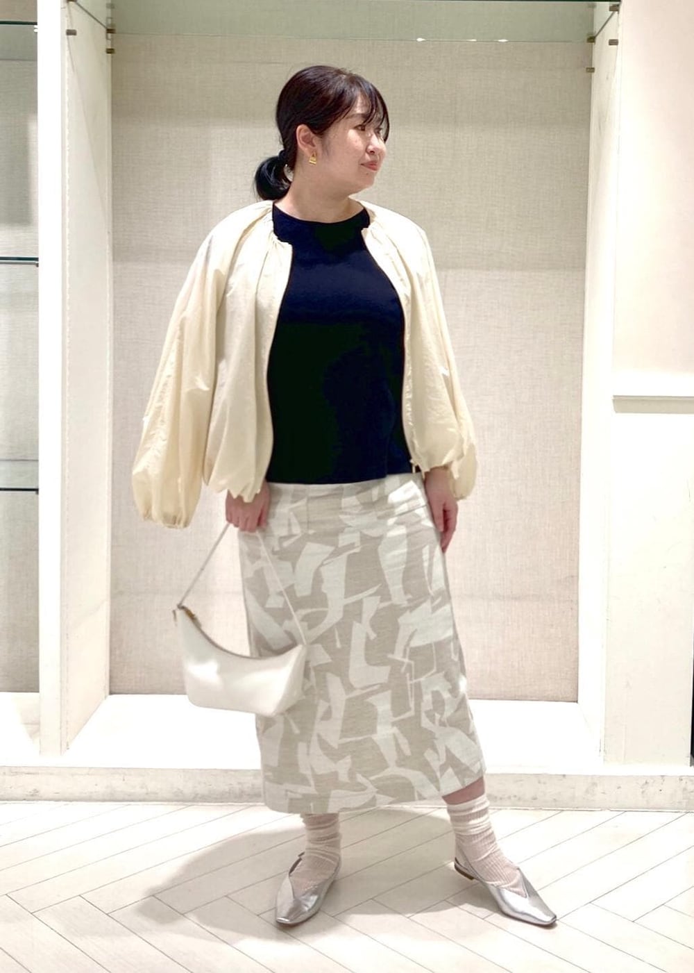 ホワイト系のハンドバッグ、シルバー系のパンプス、ブラック系のニット/セーターを着用したレディースの春コーディネートの2枚目の写真