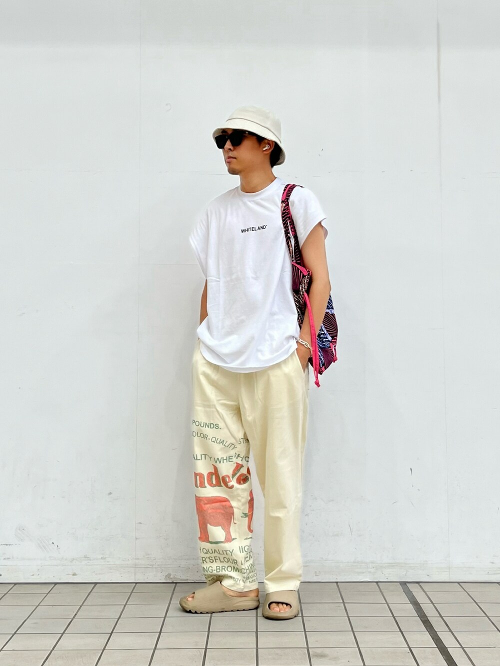 ホワイト系のタンクトップ、ホワイト系のパンツ、ベージュ系のサンダルを着用したメンズの夏コーディネートの2枚目の写真