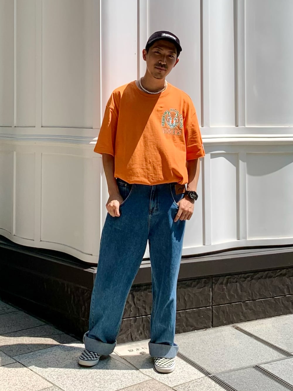 オレンジ系のTシャツ/カットソー、ブルー系のデニムパンツ、ブラック系のスリッポンを着用したメンズの夏コーディネートの2枚目の写真