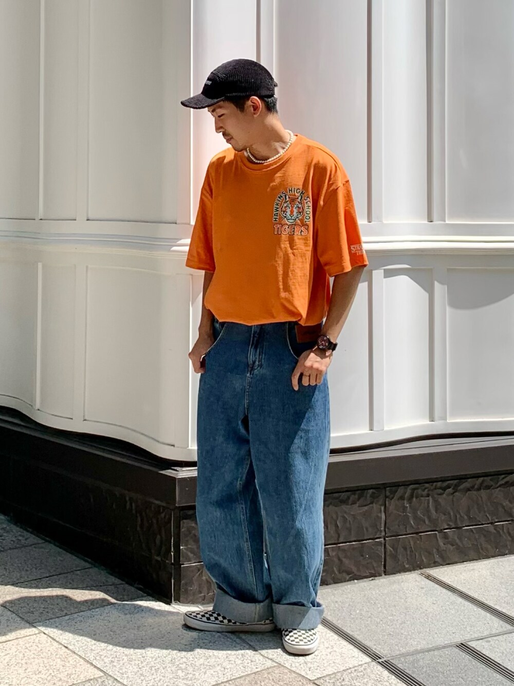 オレンジ系のTシャツ/カットソー、ブルー系のデニムパンツ、ブラック系のスリッポンを着用したメンズの夏コーディネートの3枚目の写真